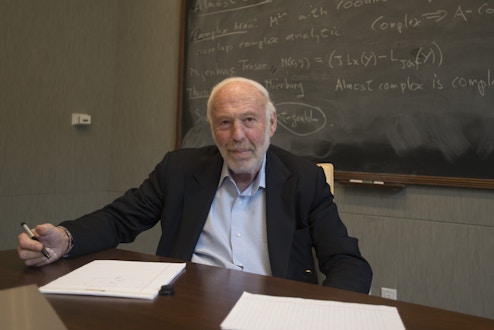 Jim Simons sitting in front of chalkboard.