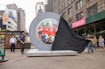 A large black sheet is being pulled of a silver circular structure in New York City